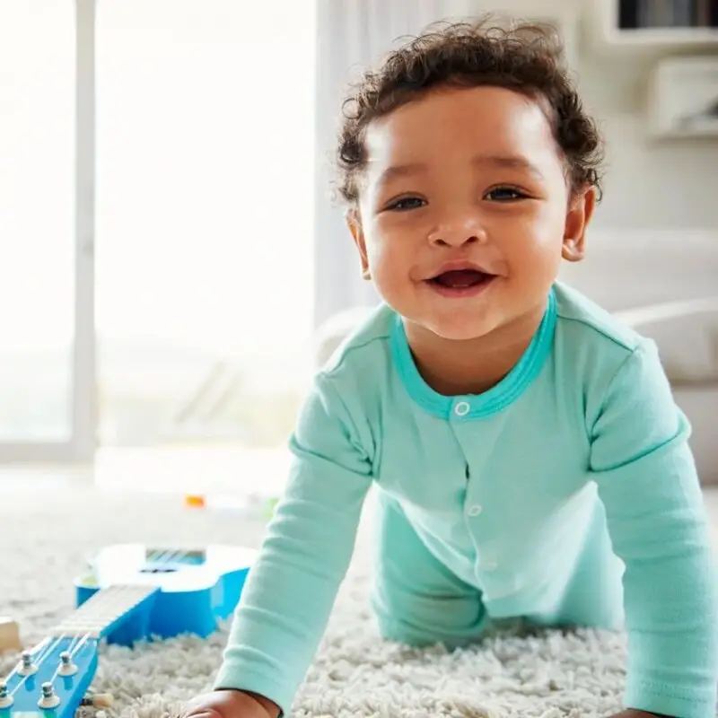 A baby is smiling while sitting on the floor.