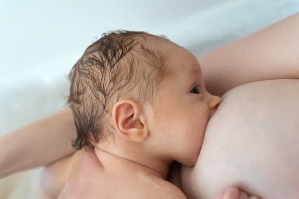 A baby is sucking on the breast of another woman.