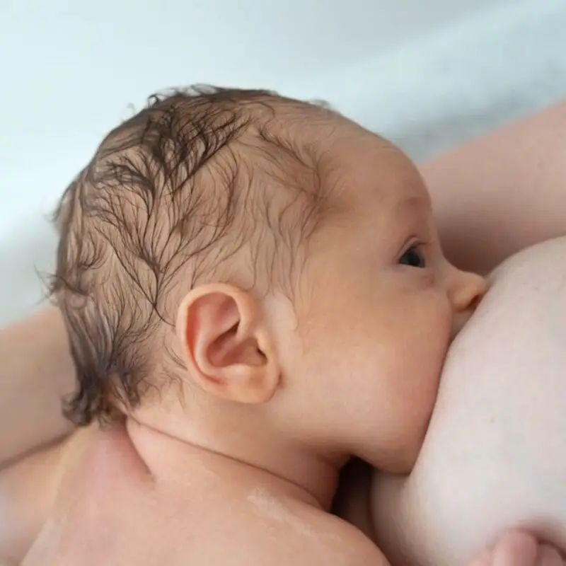 A baby is sucking on the breast of another woman.