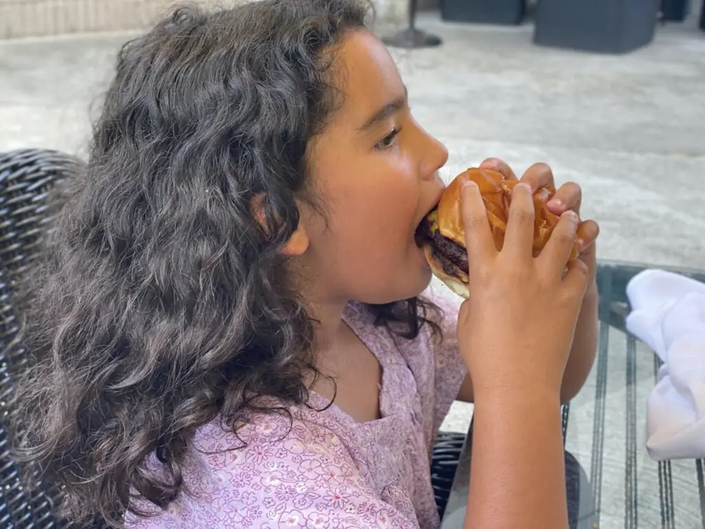 A girl eating a large sandwich on top of a bun.