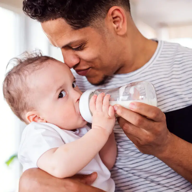 A man holding a baby and drinking from a bottle.