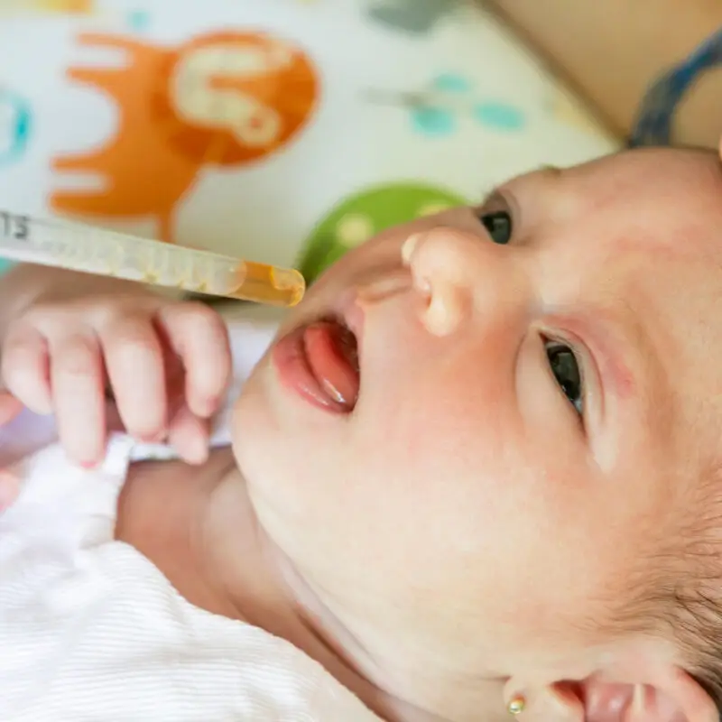 A baby is laying down and brushing its teeth.