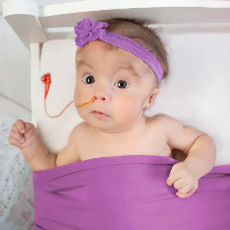 A baby with a purple blanket and a tube of oxygen in its mouth.