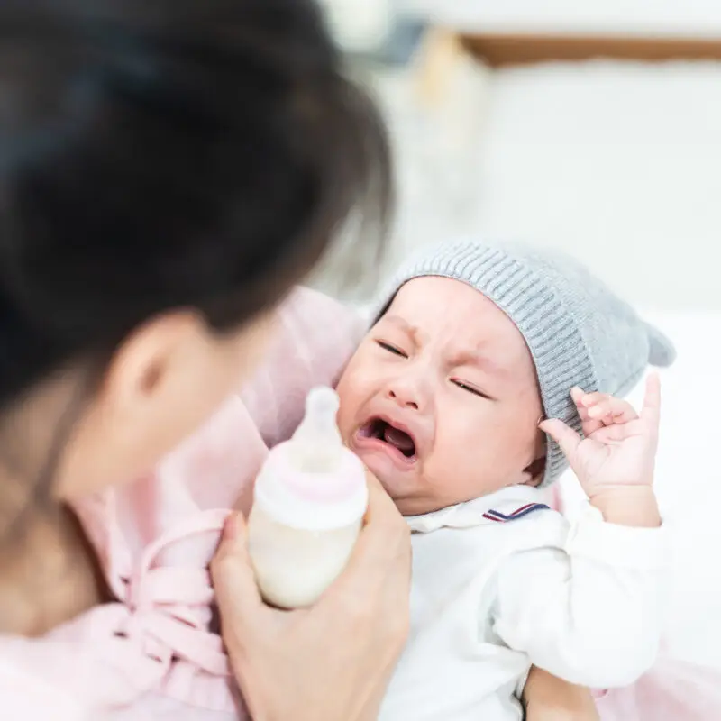 A woman holding a baby and bottle in her hand.