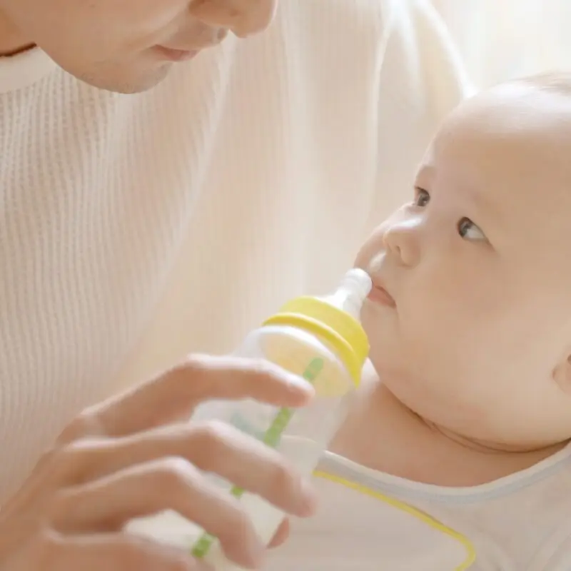 A woman is holding a baby and drinking from a bottle.