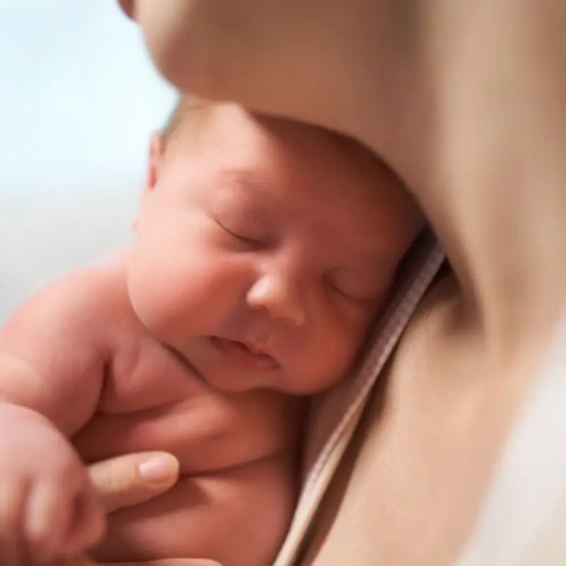 A baby is wrapped in a blanket and held by its mother.