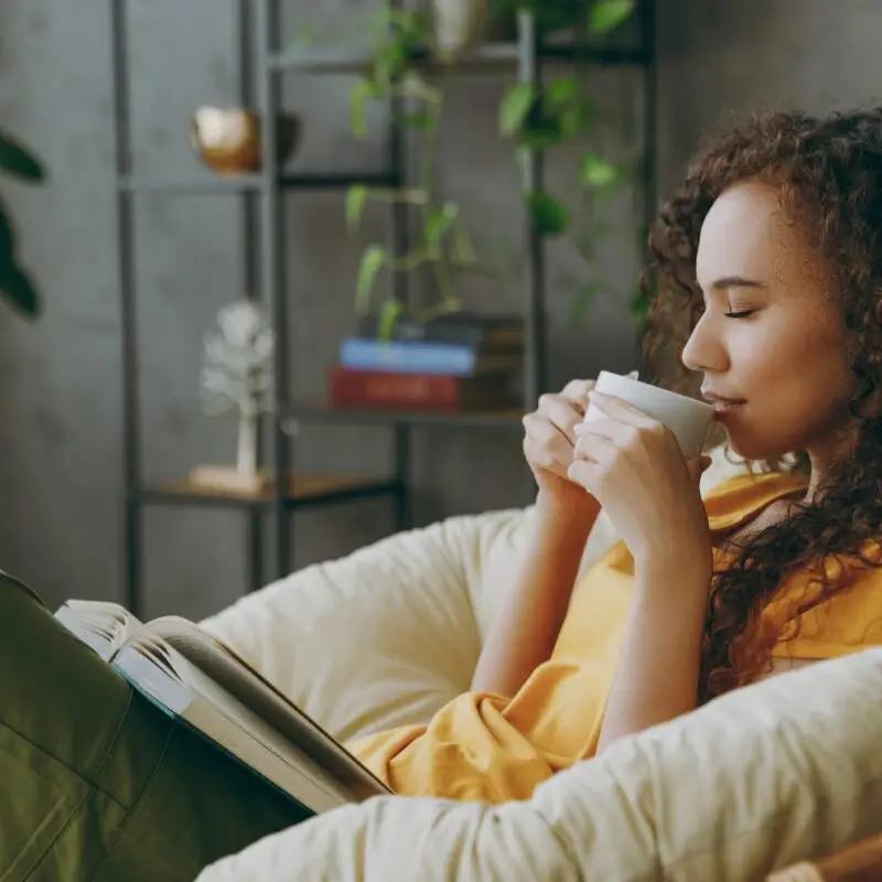 A woman sitting on top of a couch drinking coffee.