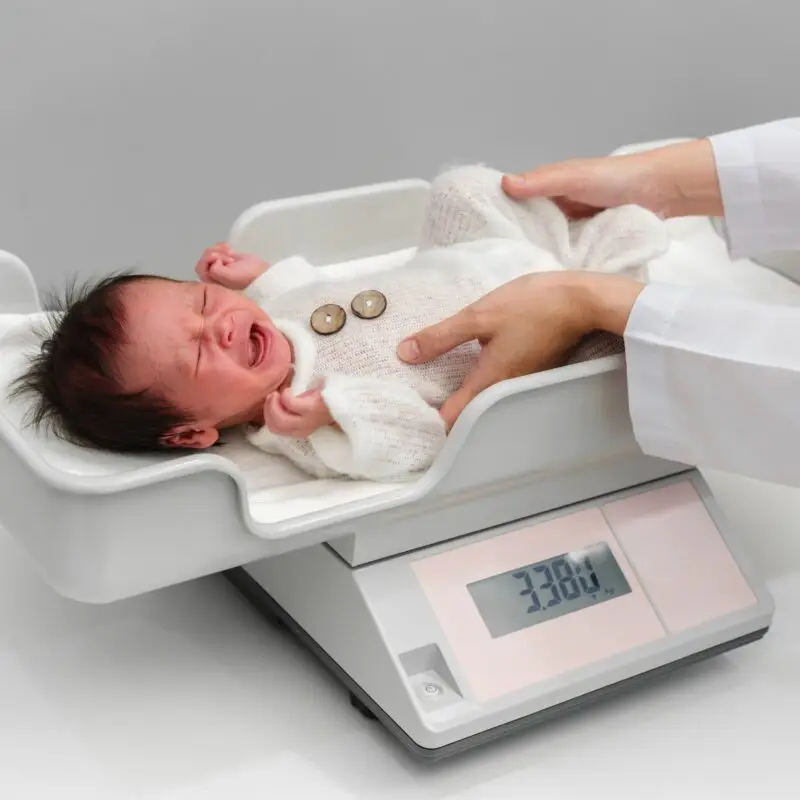 A baby is weighed on the scale by an infant.