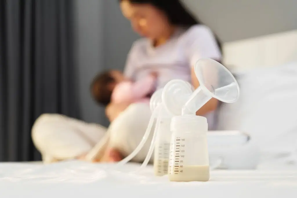 A woman is holding her breast milk while sitting on the bed.