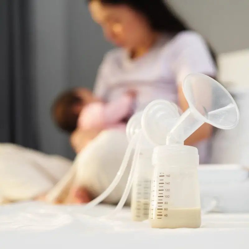 A woman is holding her breast milk while sitting on the bed.