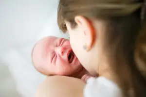 A baby is crying while being held by an adult.