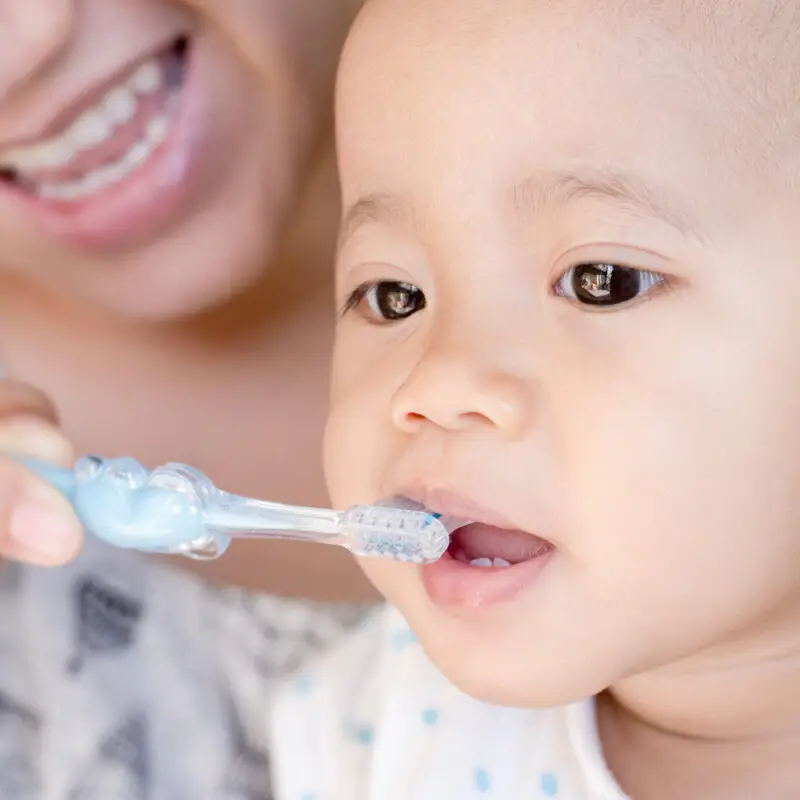 A baby is brushing its teeth with an adult.