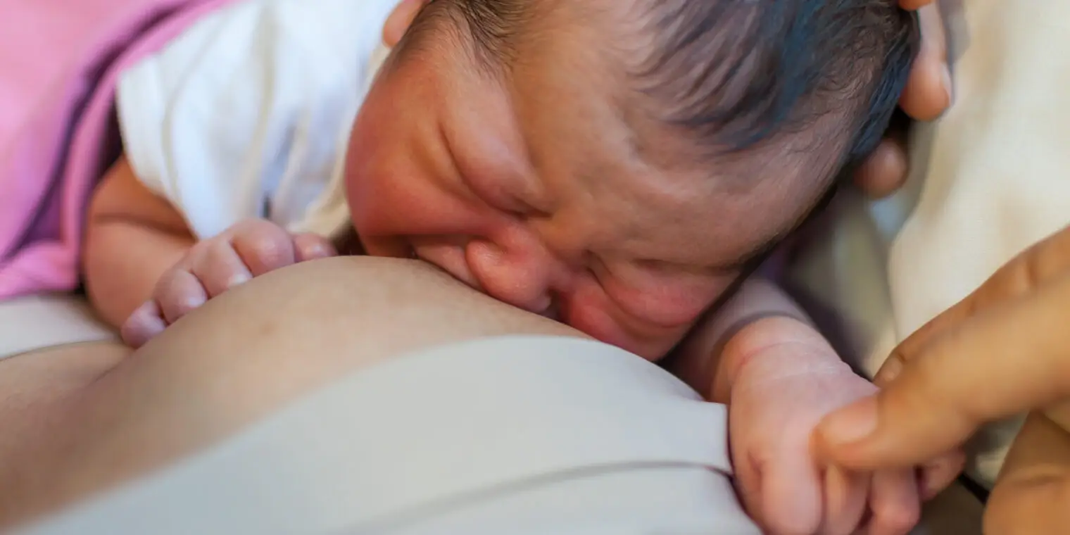 A baby is laying down and nursing her mother.