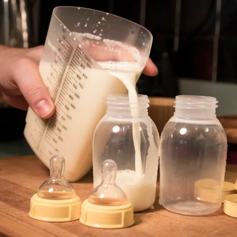 A person pouring milk into a baby bottle.