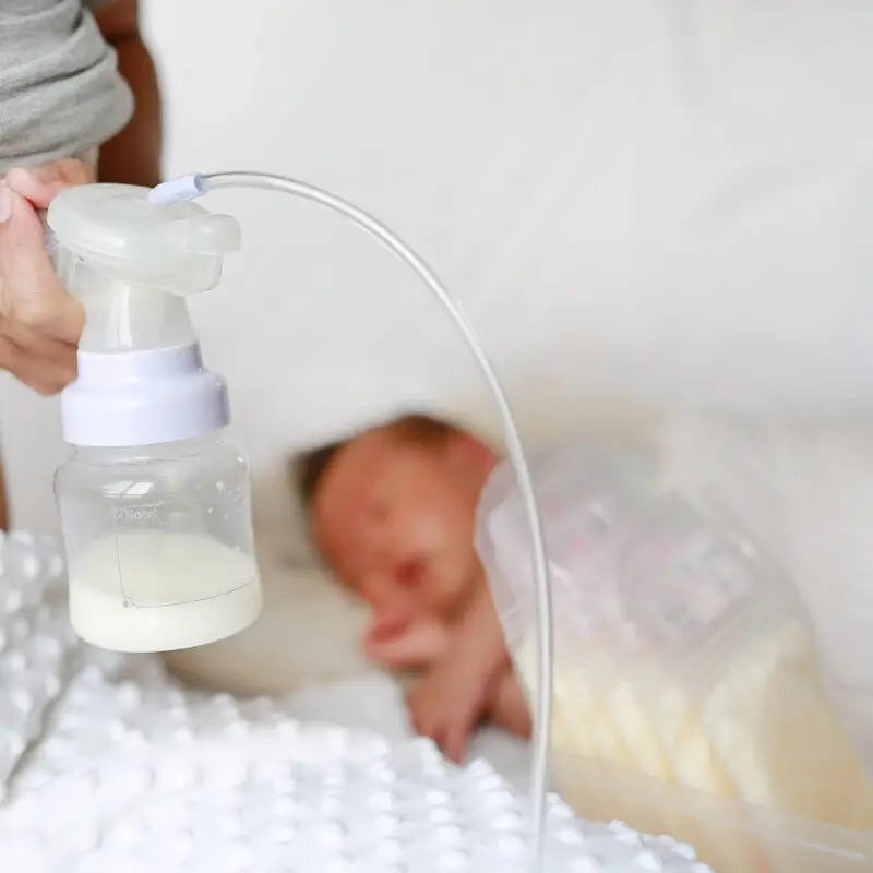 A baby is laying down while mom pumps breast milk.