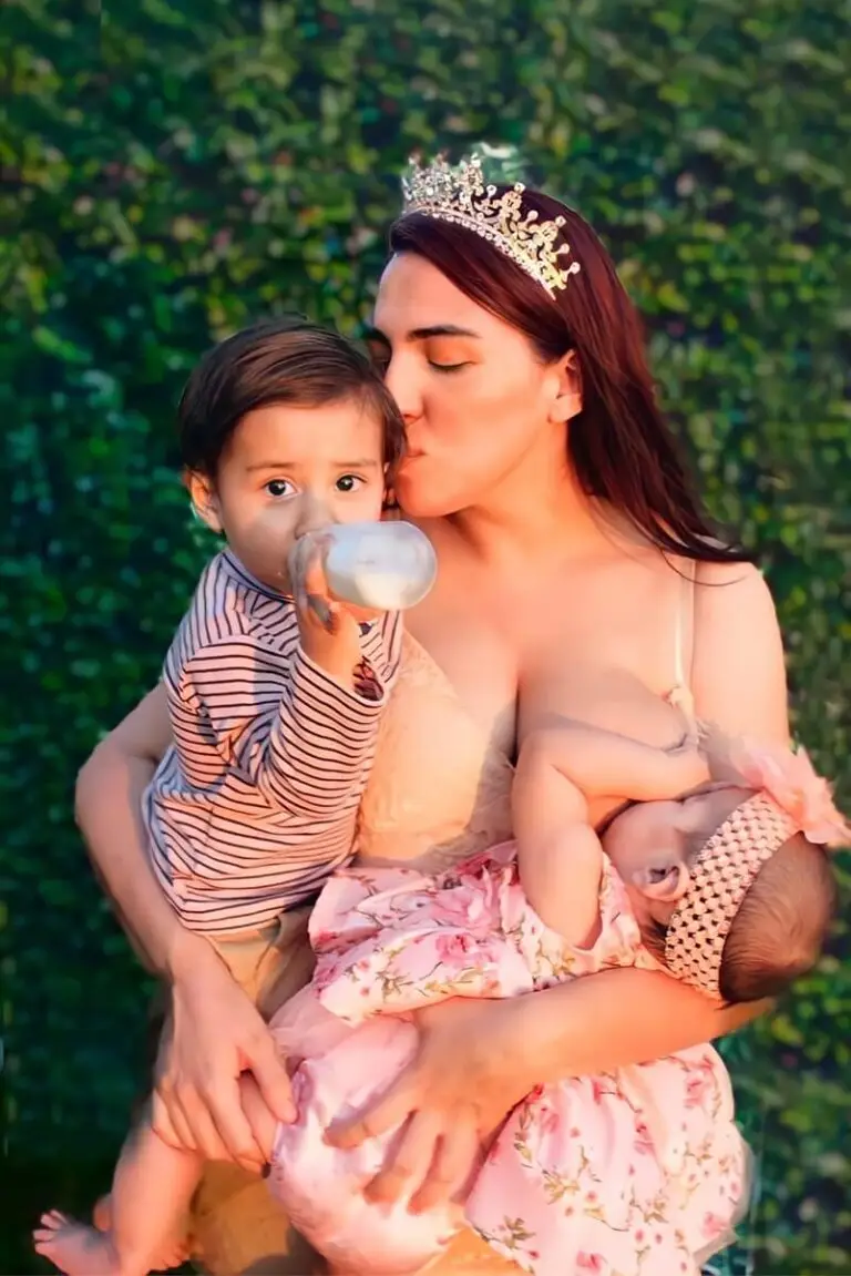 A woman holding two children and kissing her breast.